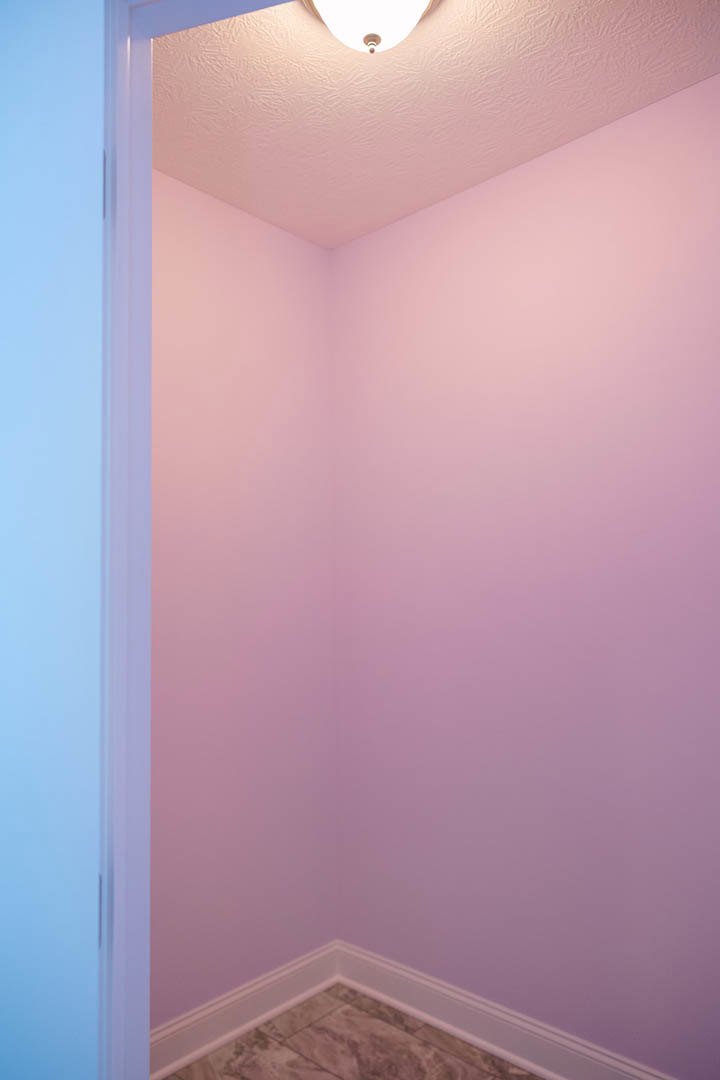 Corner of a room with pastel pink plaster walls, white ceiling, and a modern light fixture