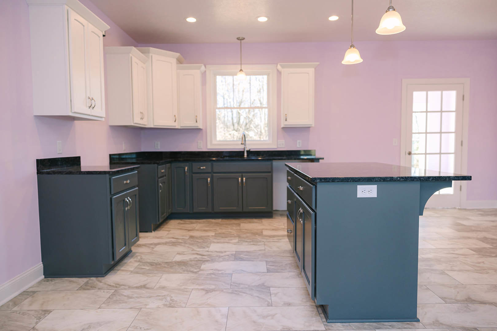 Kitchen with bold purple walls, white cabinets, black countertop island, glass-paneled white door, window with overhead light fixture, and contrasting black lower cabinets on light