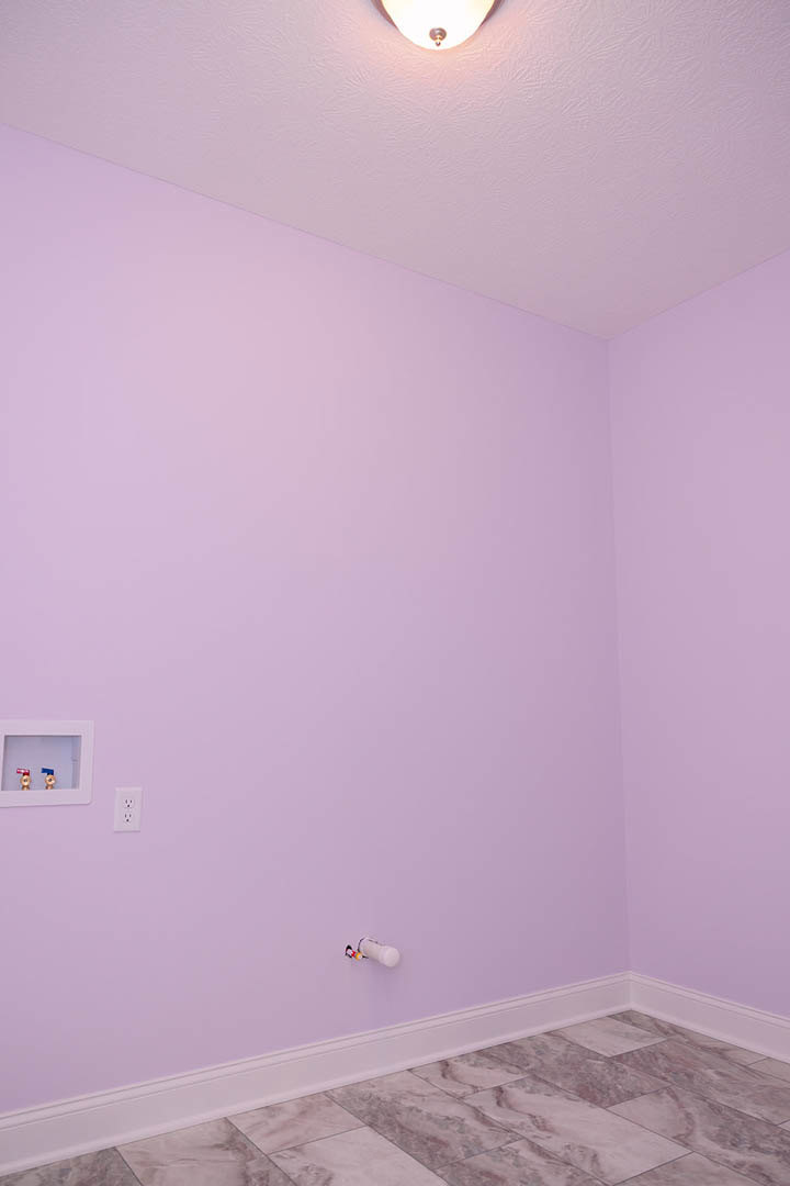 Purple accent wall with white floating shelf, ceiling-mounted light fixture, tile flooring, and wall sconce in a modern residential room.