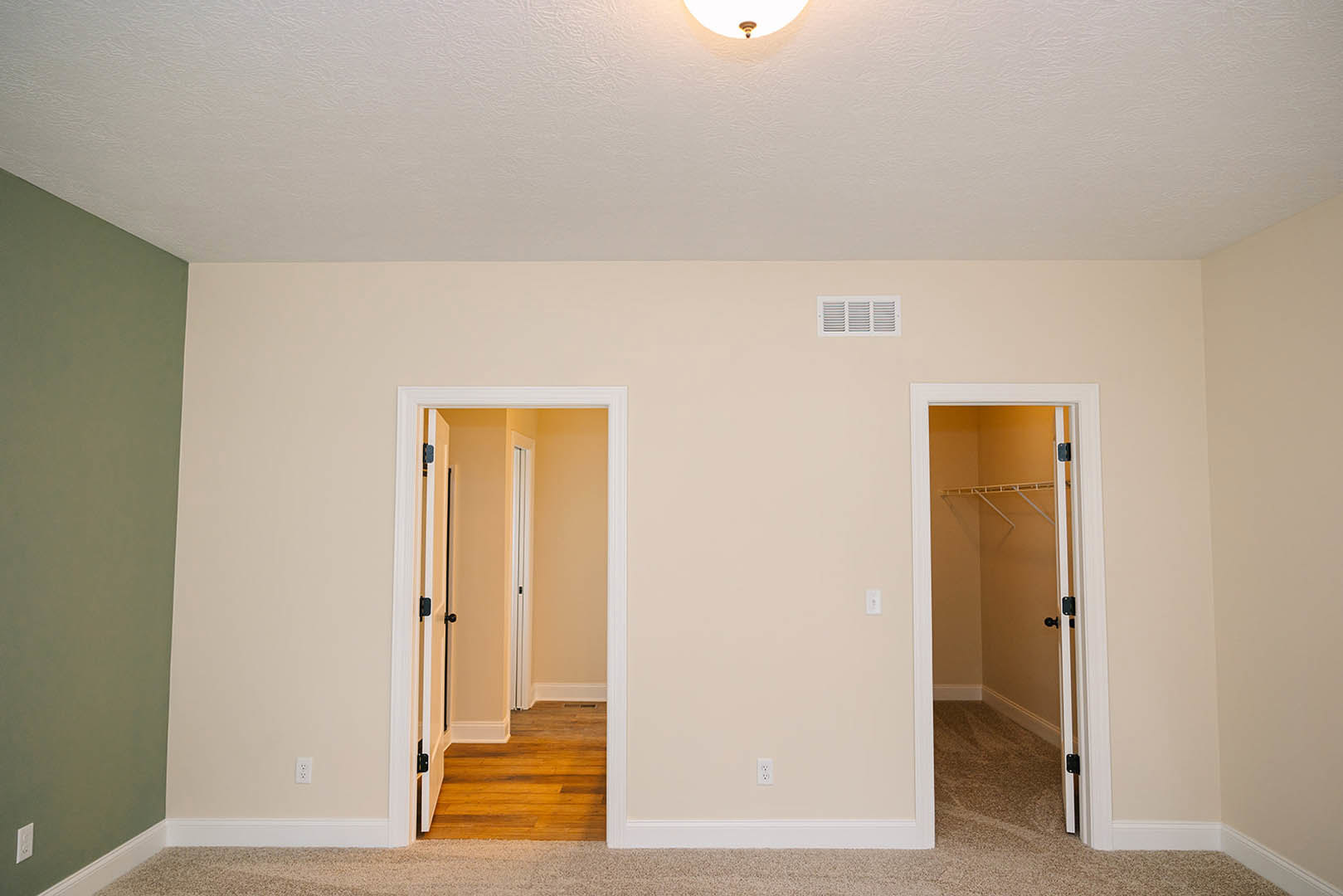 White closet door and hallway doors with wood flooring, green walls, white trim, and a vent near the baseboard