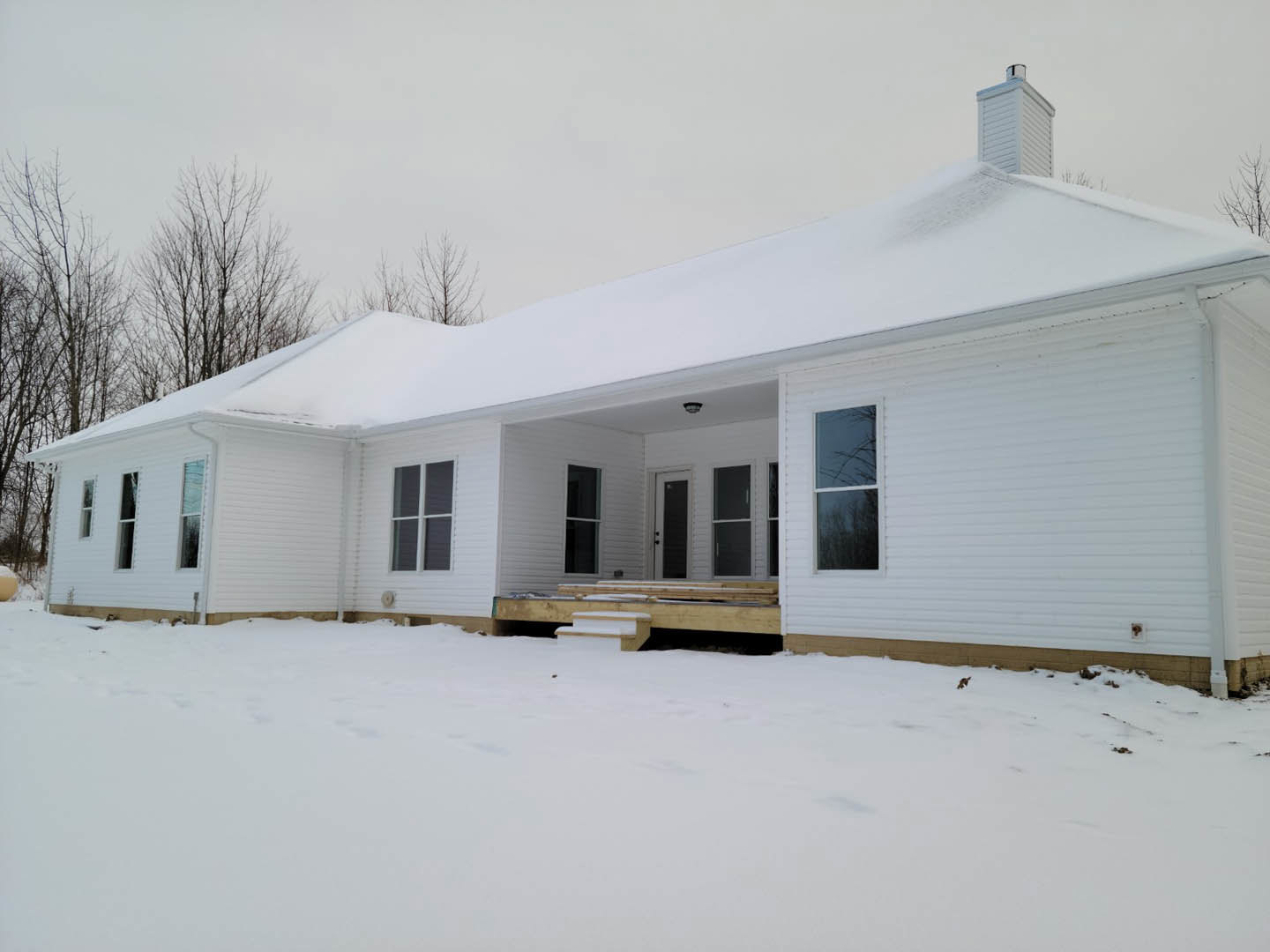 White cottage-style home with snow-covered ground, white-framed windows, light siding, and a cross atop the roof against a winter sky