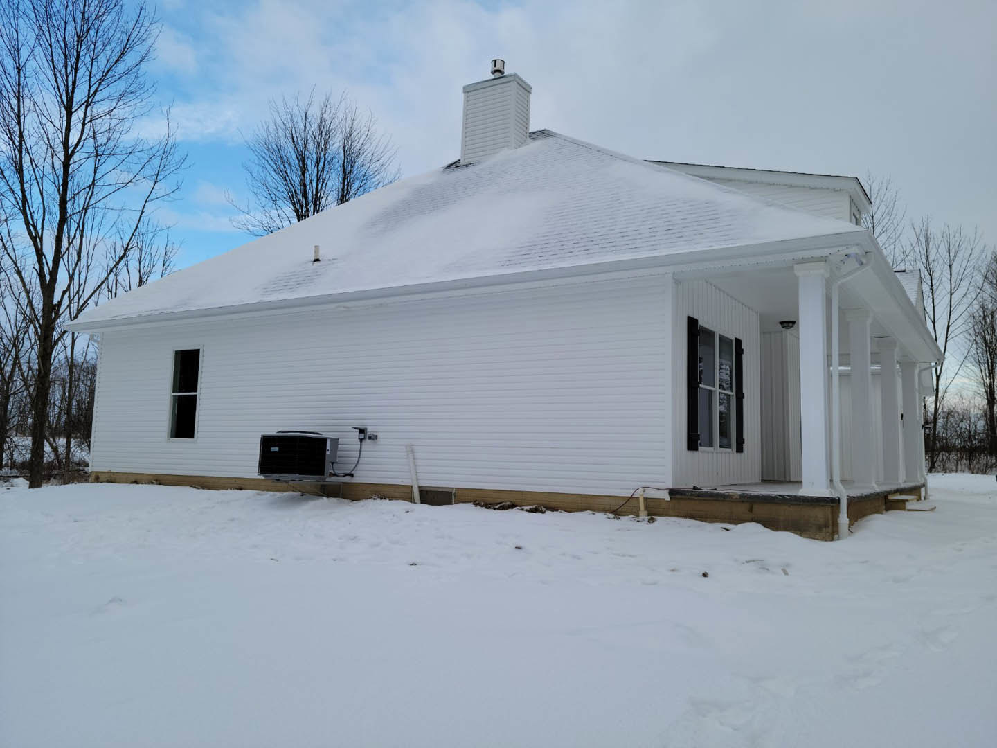 Two-story home with white siding and snow-covered roof, bare tree in front yard, car parked near snow-covered driveway, white-framed windows, overcast winter sky