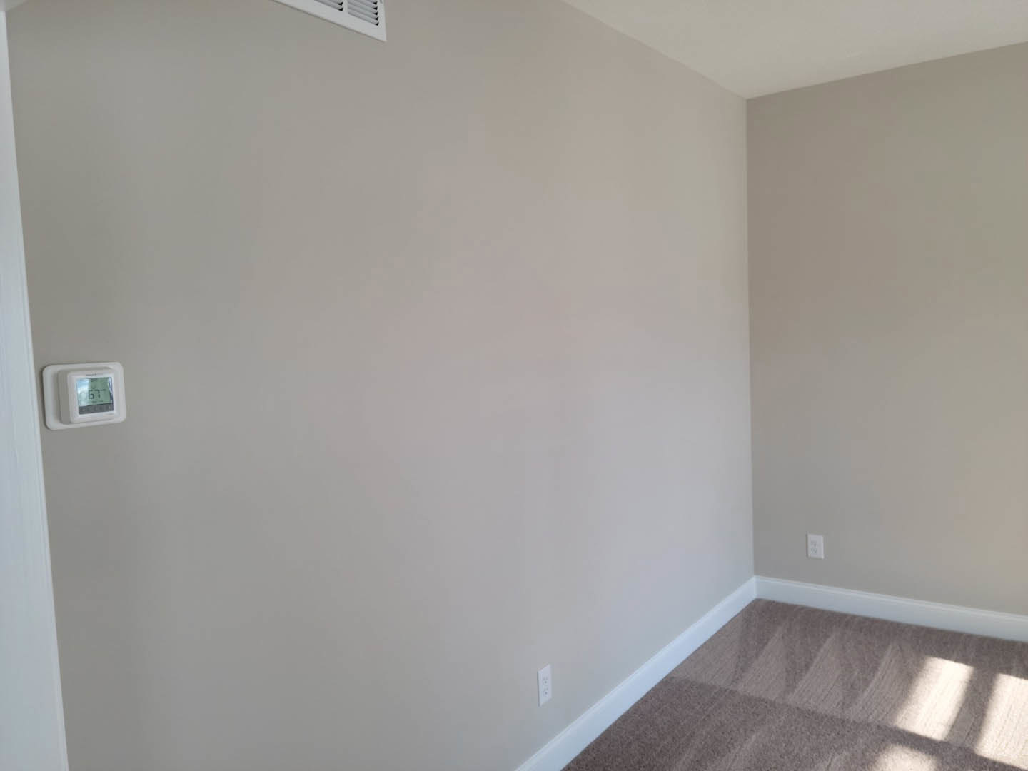 White carpeted floor, white walls with matching baseboards, white ceiling, and a close-up of a digital thermostat mounted near a white-framed doorway.
