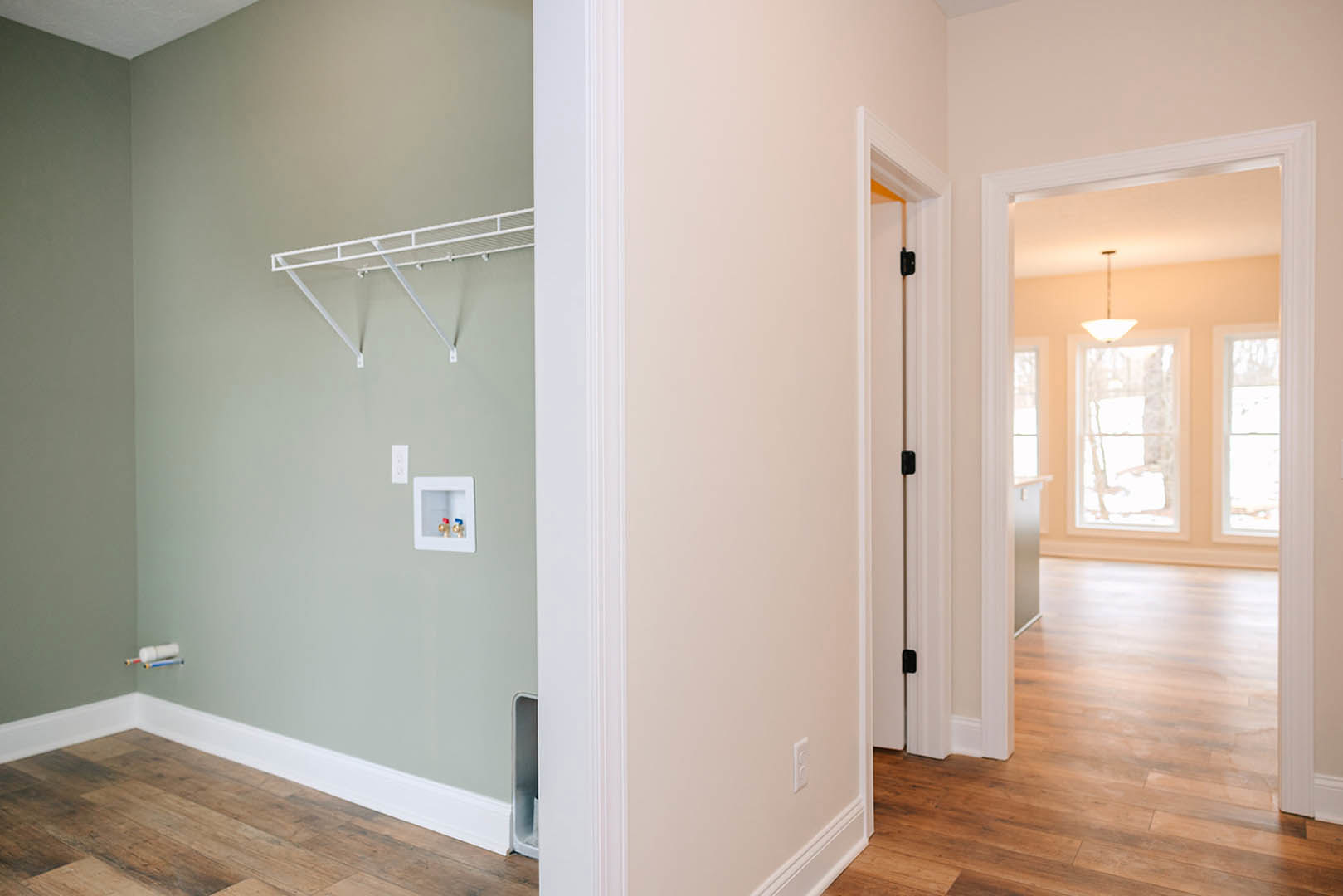 Hallway with smooth white plaster walls, light wood flooring, white baseboards, built-in white shelf, and a window with a white frame