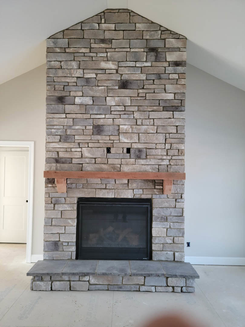 Stone fireplace with wood mantel, brick accent wall, black fire screen, and white door with black hardware in a cozy living room.