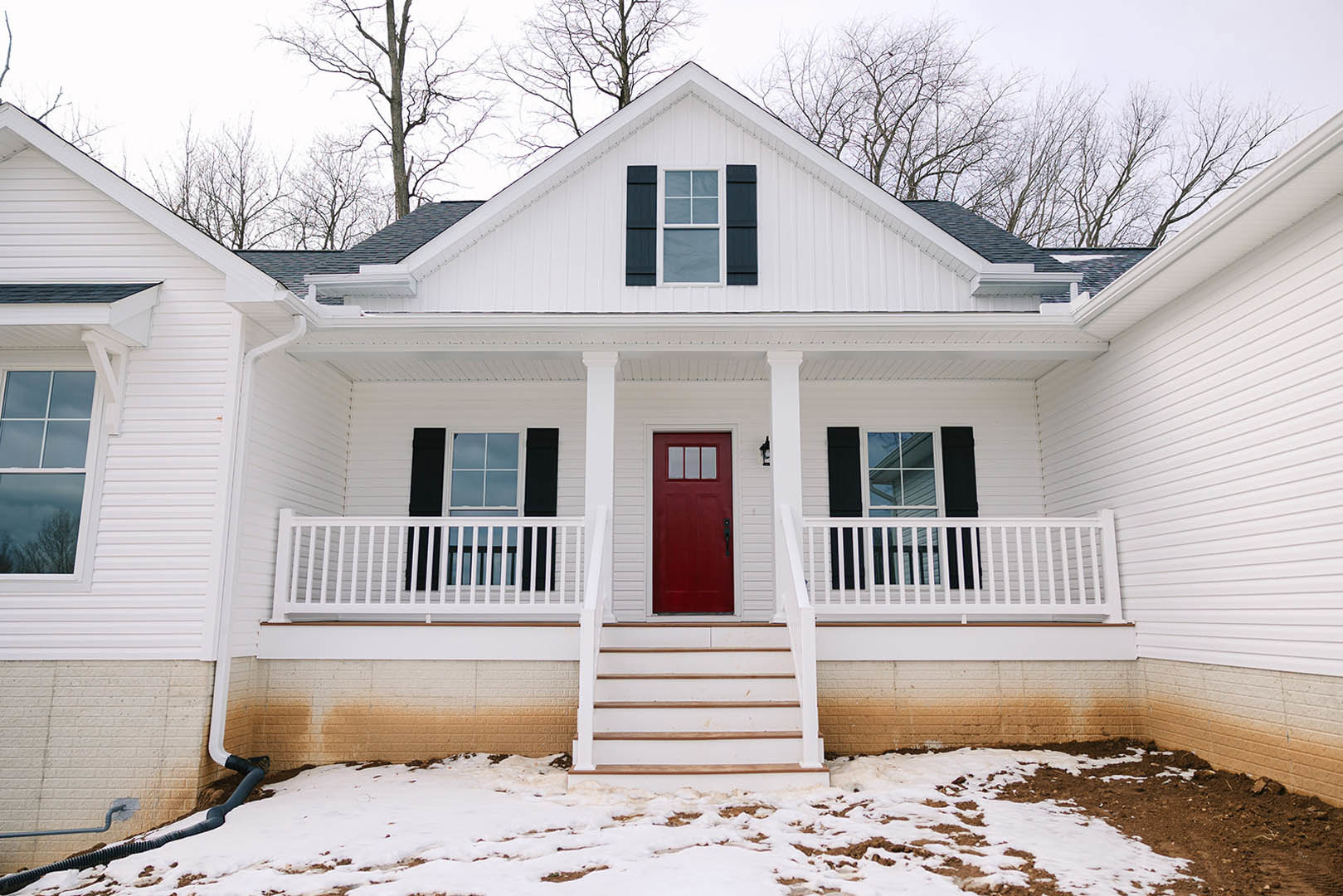White siding house with two red doors, snowy front yard, white staircase, and windows on the porch.