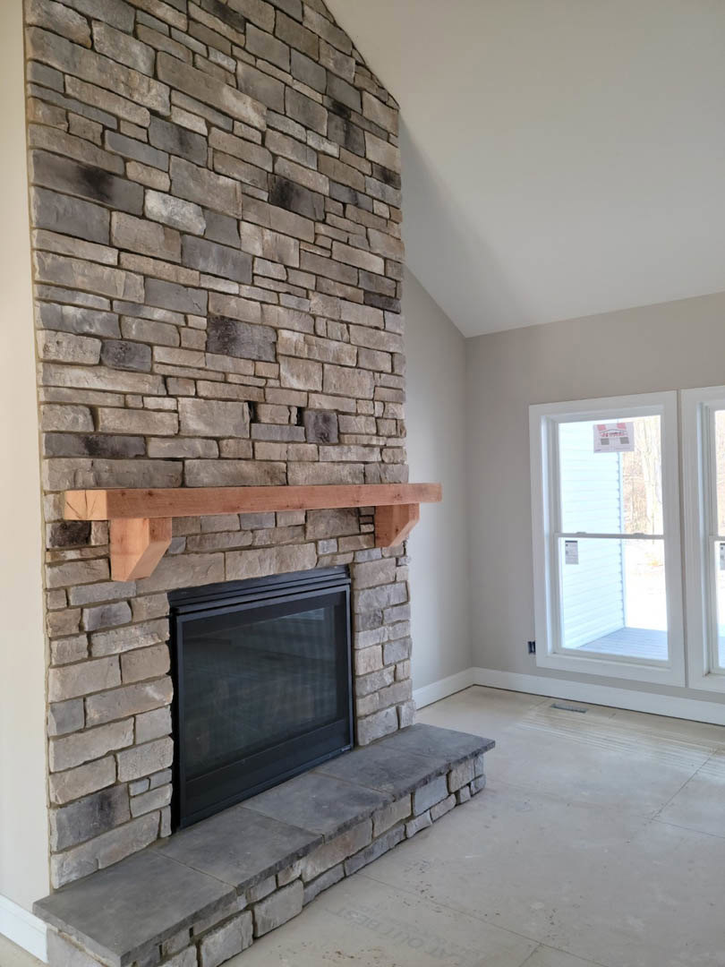 Stone fireplace with black metal door, wood mantel shelf, brick wall backdrop, and nearby window with sign visible