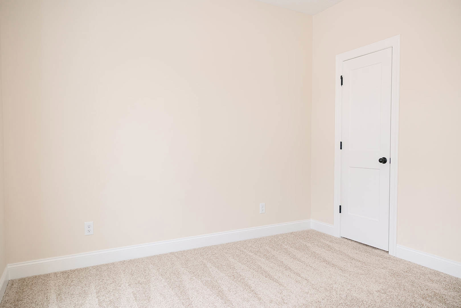 White paneled door with black knob set in a room with light carpeted floor and smooth white walls