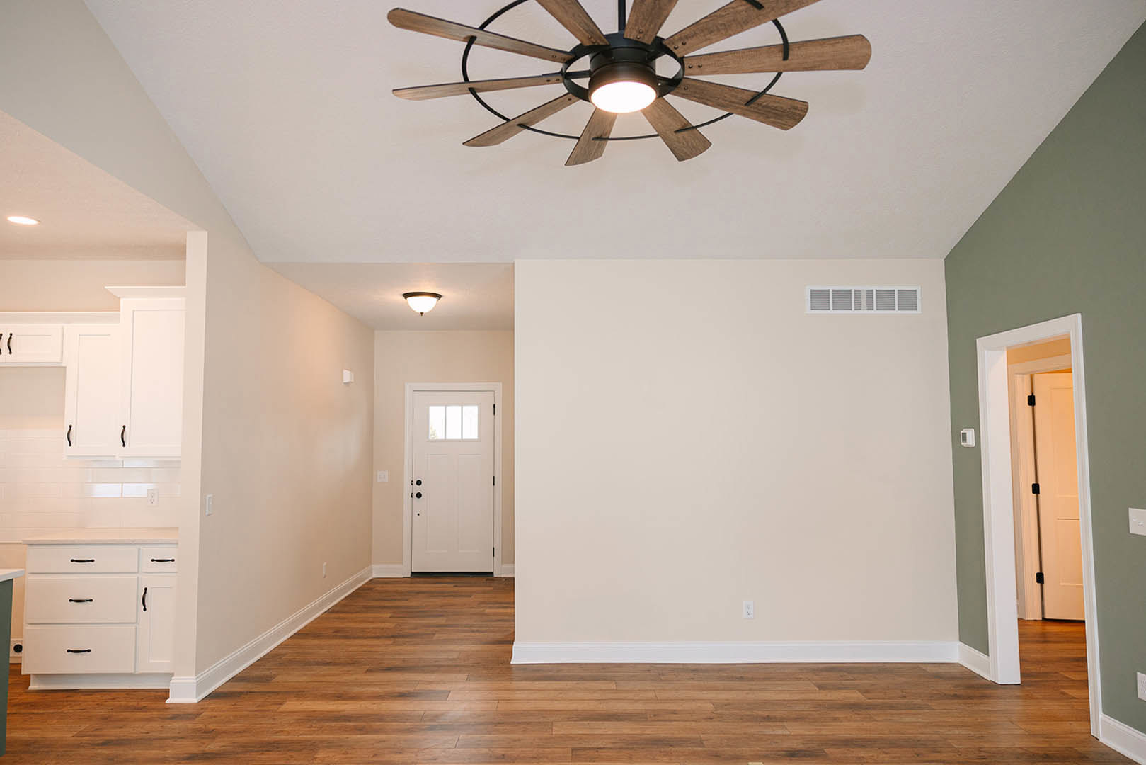 Ceiling fan with light fixture above wood flooring, white door with glass window, white cabinetry with black handles, wall vent, and close-up of door panel