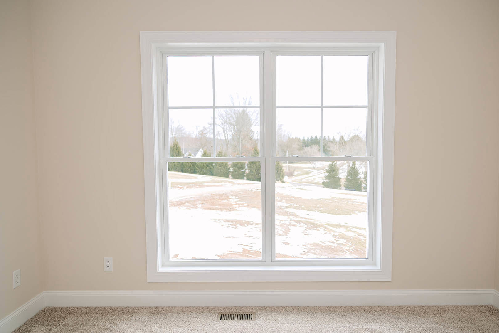 Large window with white trim overlooking snowy field, floor vent below, neutral walls and minimalist interior finishes