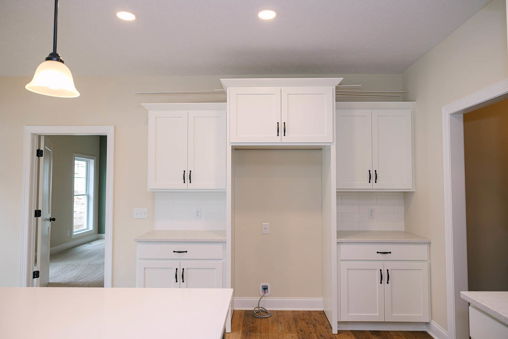 White kitchen cabinets with black handles, wood plank flooring, white countertop, and a window with natural light.