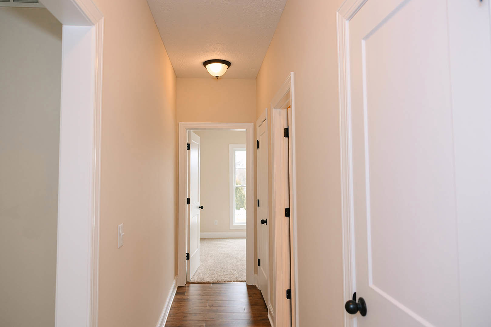 Hallway with white paneled doors, black hardware, and medium-toned hardwood flooring; white walls and ceiling with recessed lighting fixtures