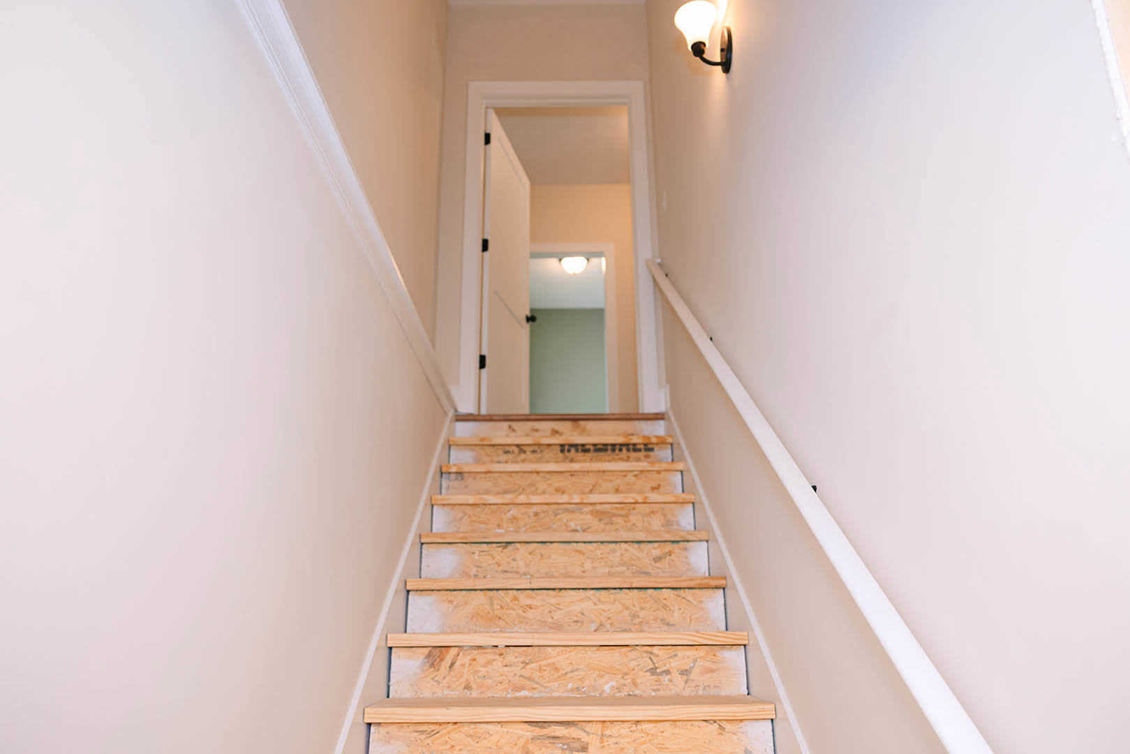Staircase with plywood side panels, white door with black knobs, wall-mounted light fixture, close-up views of wood surfaces and shelving