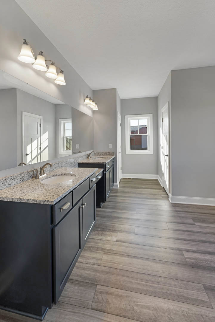 Bathroom with marble countertop, wood flooring, white-framed window, ceiling row of lights, white door letting in natural light, close-up of chrome faucet