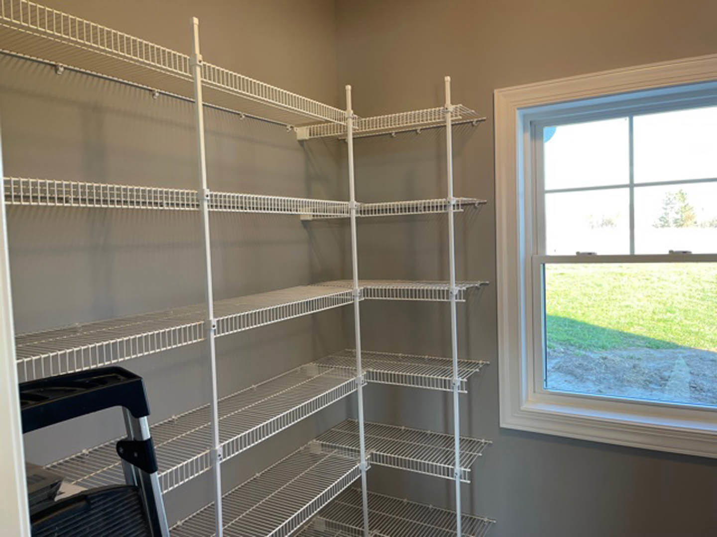 White built-in shelves along a wall in a room with a large window overlooking a grassy yard, black and silver ladder leaning nearby