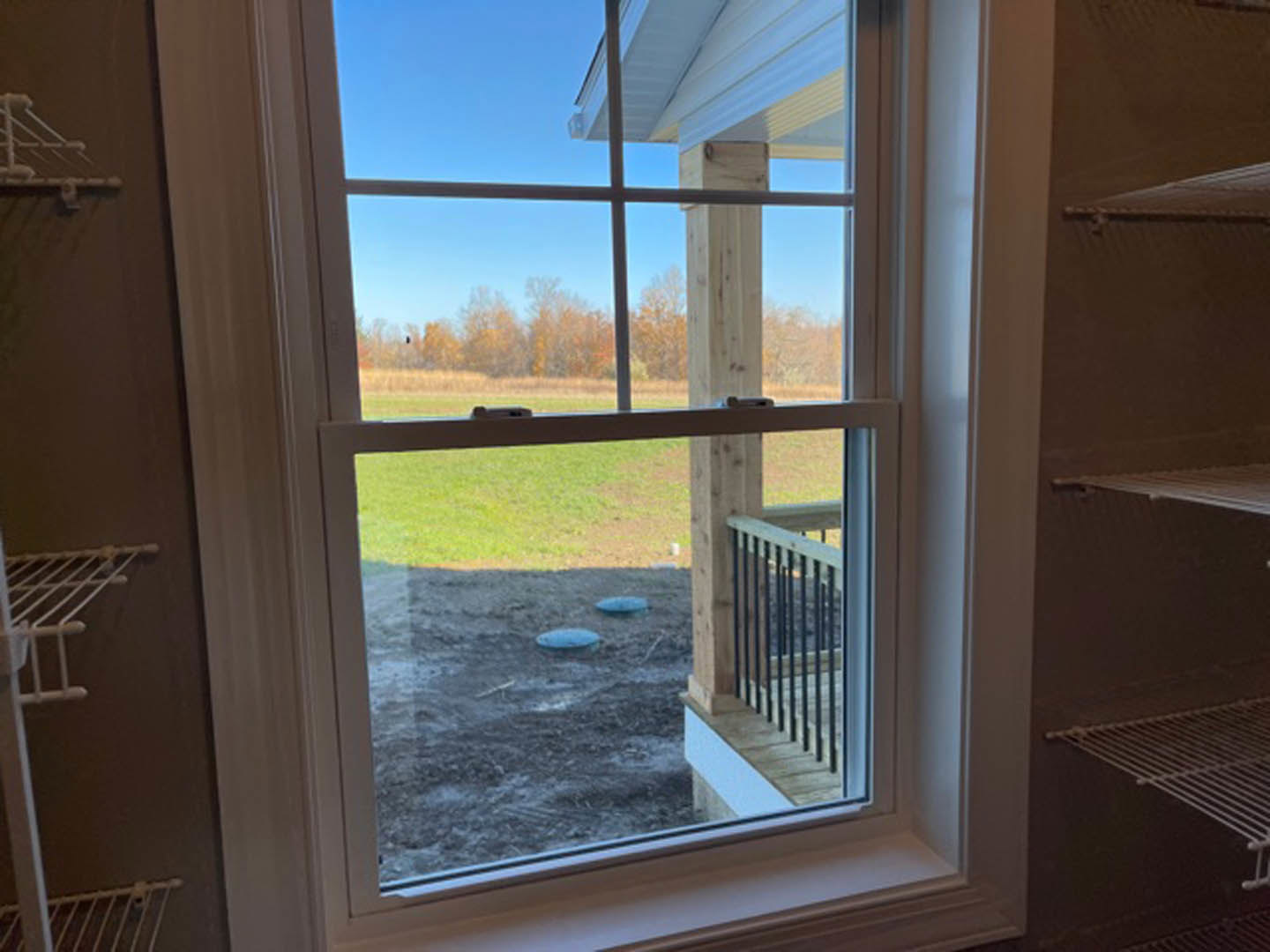 Large window with white metal grate, overlooking green grassy yard and blue sky, interior space with natural daylight
