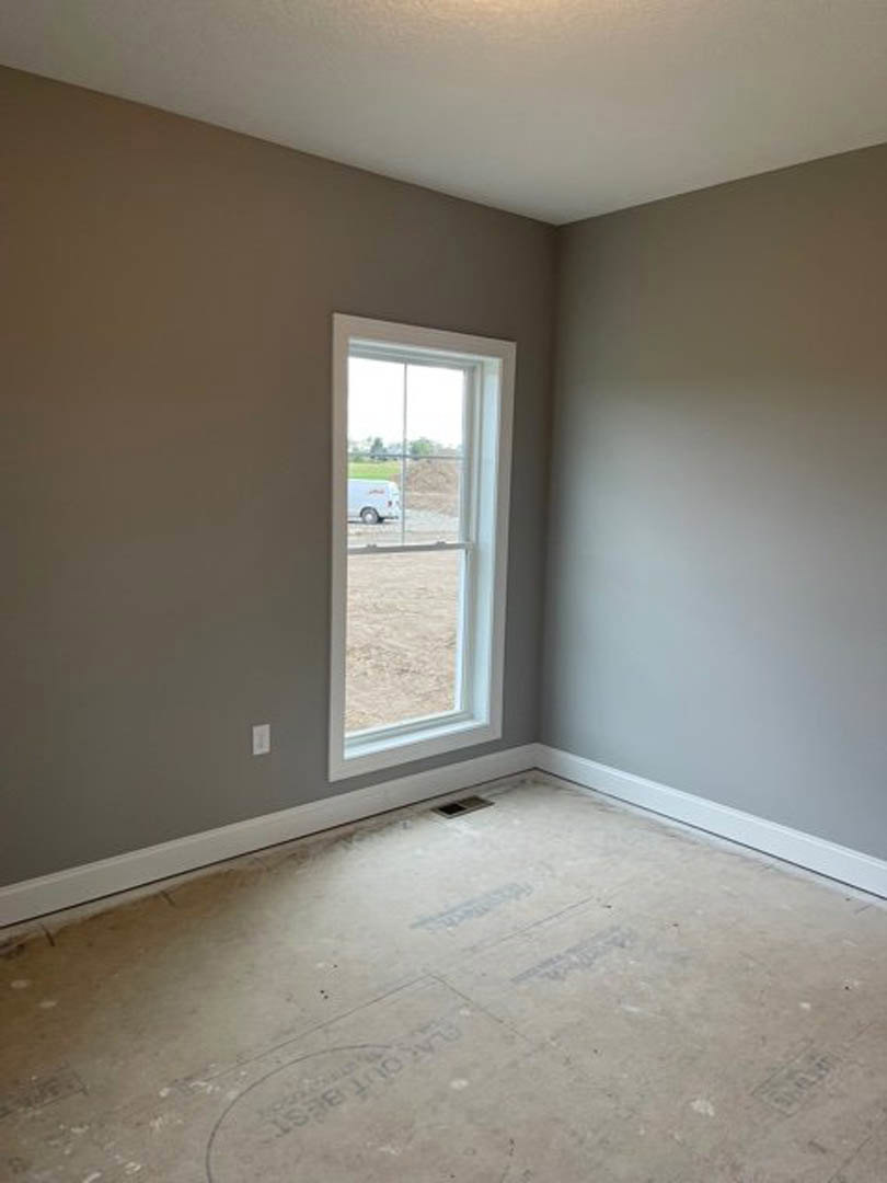 Concrete floor with circular cutouts, white plaster walls, large window overlooking parked van and distant beach, sunlight casting shadows inside.