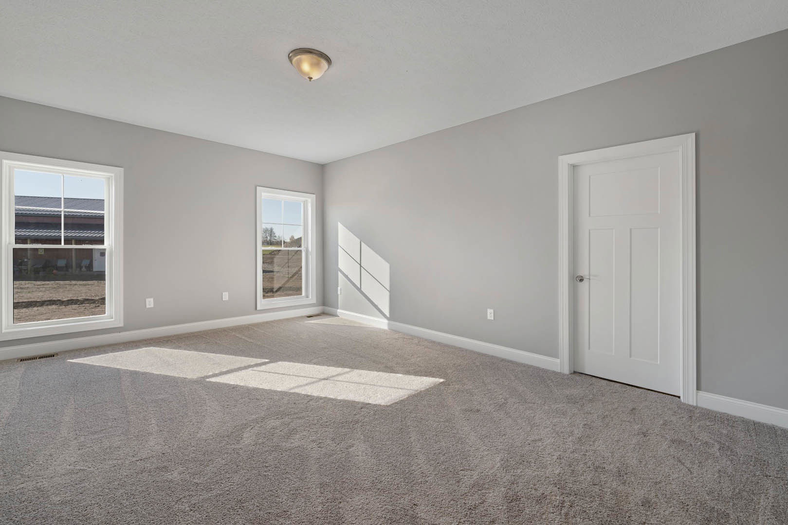 Bedroom with beige carpet, white paneled door featuring a silver handle, white walls with square molding, ceiling-mounted light fixture, and window overlooking grassy field and