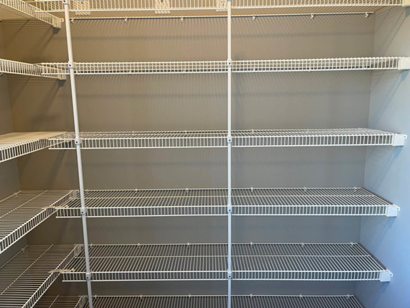 White wire shelving with metal supports installed in a closet against a white wall, brown flooring visible below.
