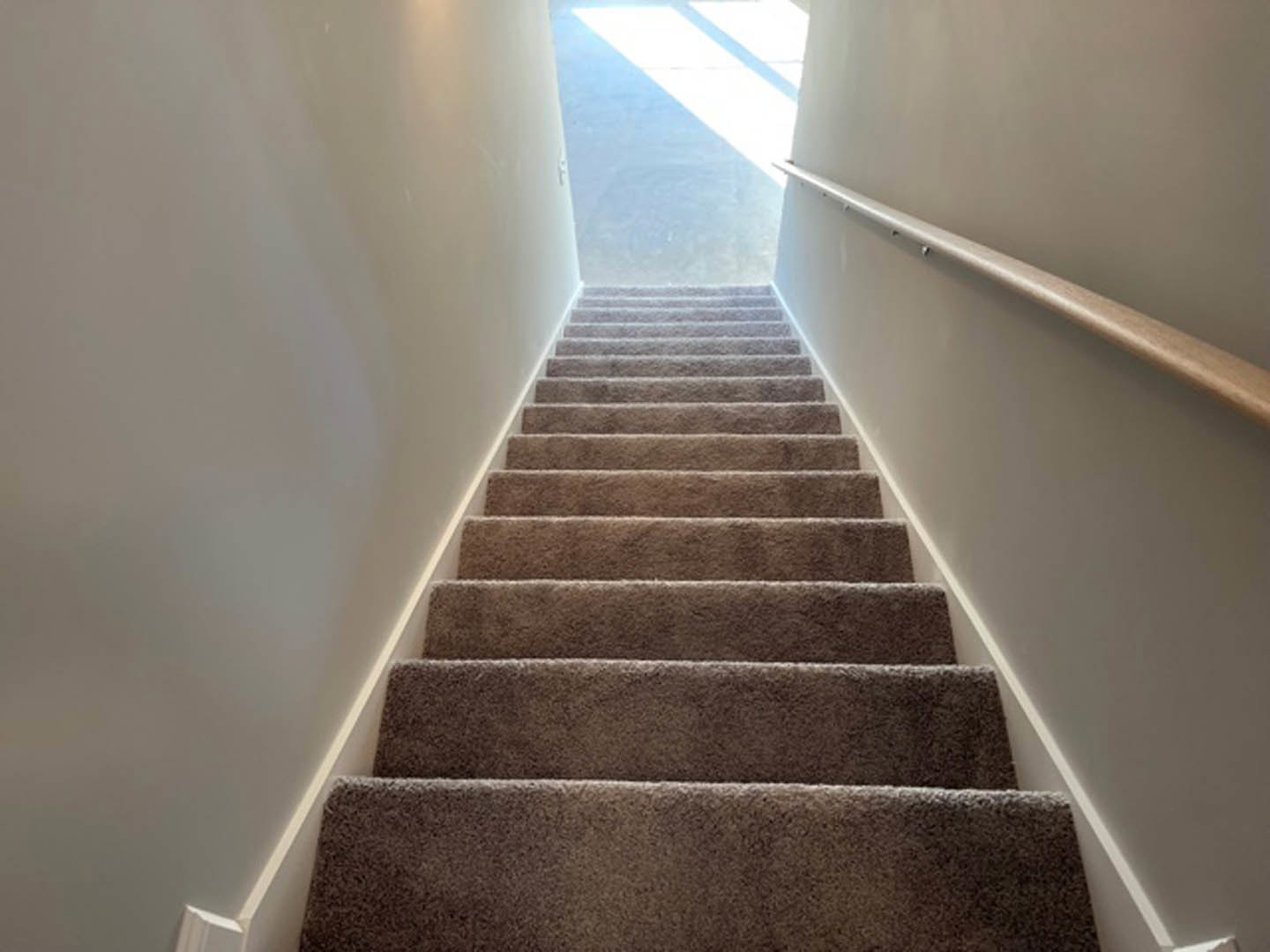 Carpeted staircase with white handrail, sunlight streaming through wall openings, casting shadows on adjacent white door and floor.