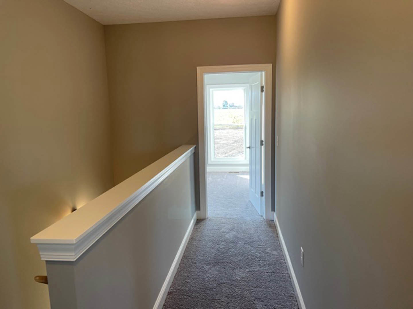 Carpeted hallway with white trim, open door leading to yard, white wall with mounted light fixture, window overlooking grassy field