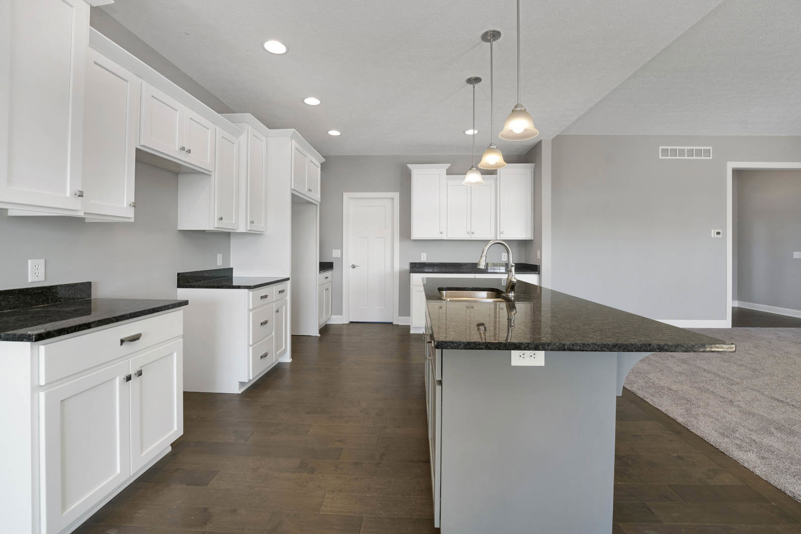 White kitchen cabinets with matte black countertops, stainless steel sink, white door with silver handle, light carpet flooring, and modern appliances.