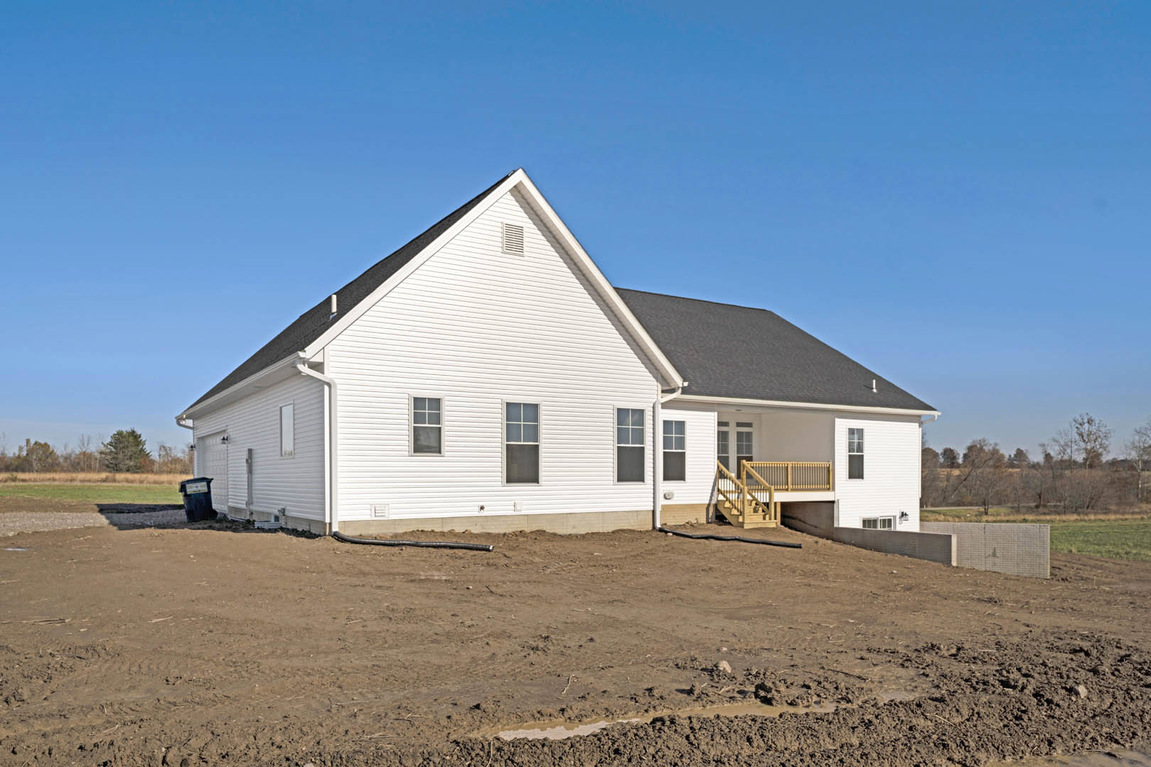 White house with black roof and white-framed windows, front staircase leading to entry, dirt area with puddle and black trash can in foreground, Rockingham Meeting House visible in
