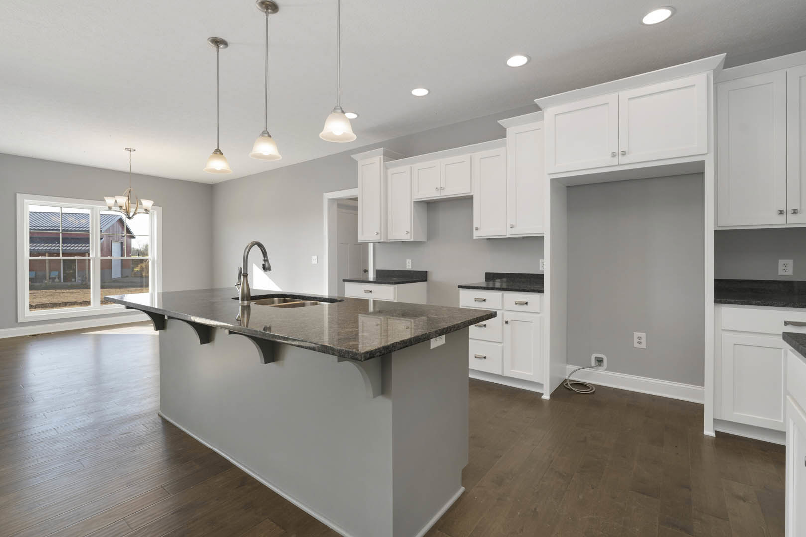 Kitchen featuring a central island with white cabinetry, black handles, quartz countertops, stainless steel sink, pendant lights hanging from the ceiling, and a window above the