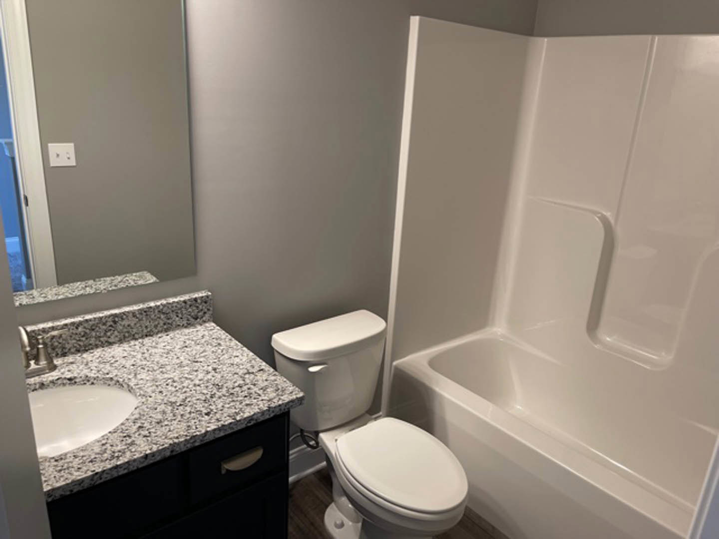 Marble countertop with oval sink, white toilet with lid up beside bathtub, light switch with black buttons on tiled wall