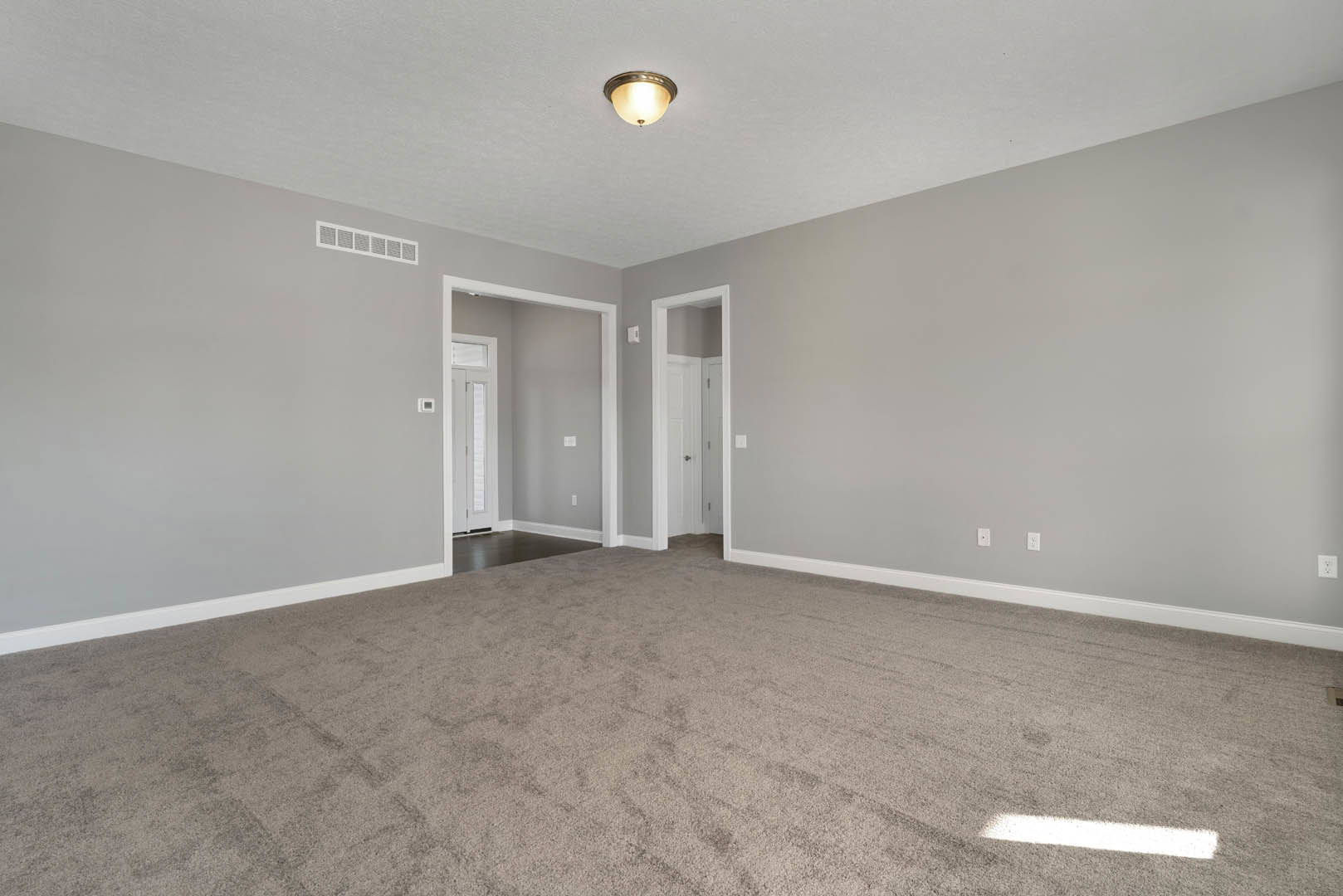 Neutral-toned carpeted room with white baseboards, ceiling-mounted light fixture, white door, and wall vent