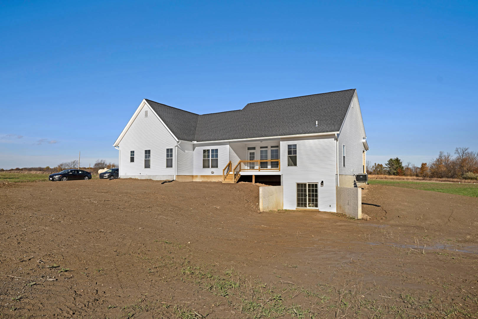Two-story house with covered porch, white railing, and stairs leading to a dirt field and parking lot; Southfork Ranch visible in the background, large windows and gabled roof
