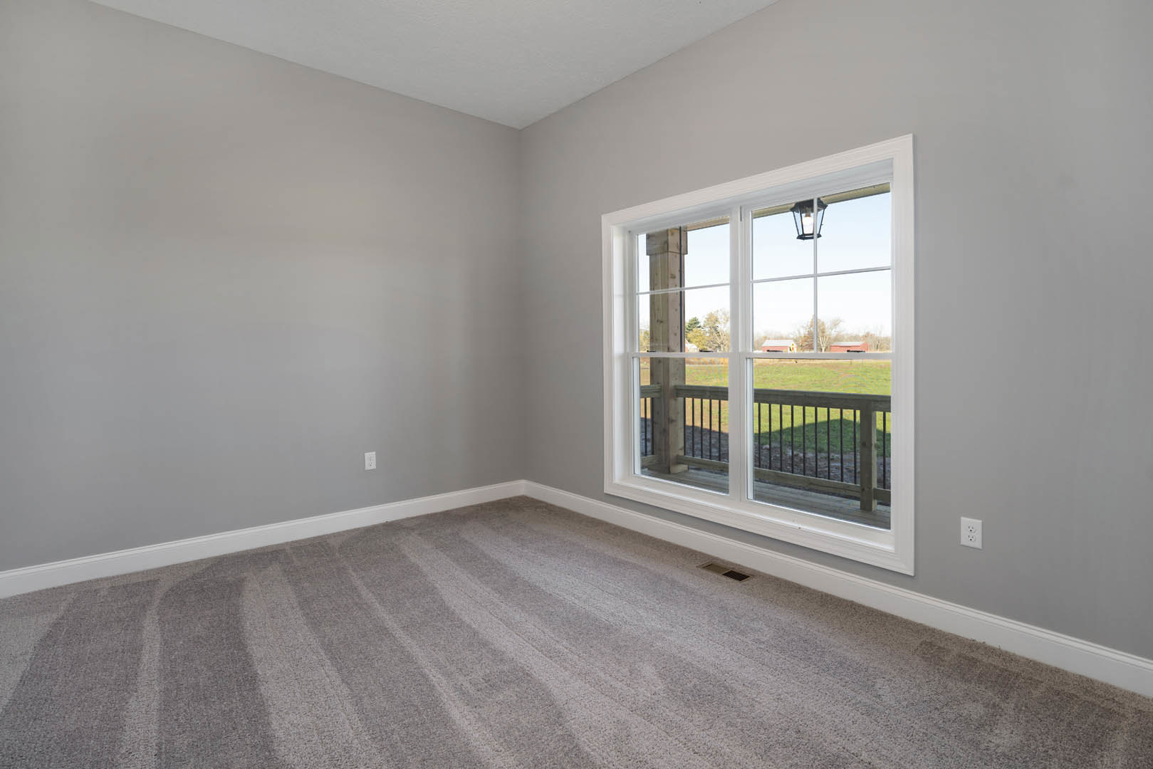 Bedroom with beige carpet, white walls, large window overlooking green lawn and porch, recessed ceiling light