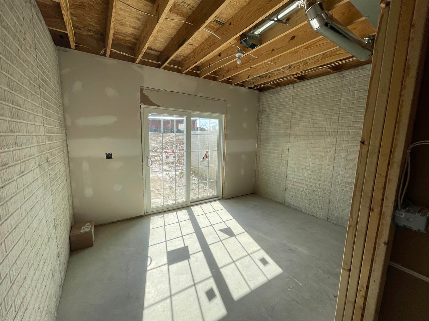 Modern interior room with plaster walls, tile flooring, a standard door, and a sliding glass door allowing daylight; window shadows cast across the concrete floor, brown box with