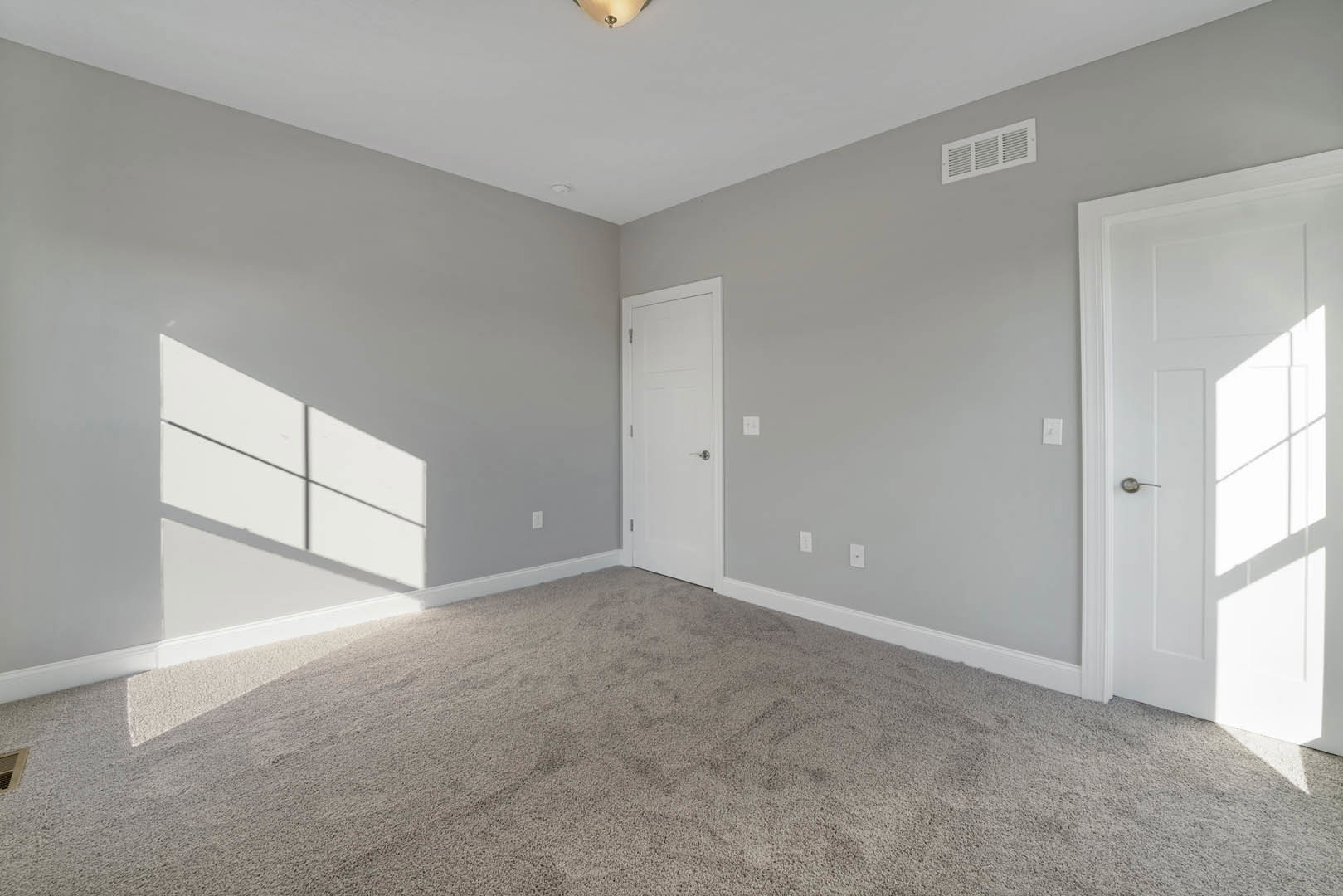 Carpeted room with white walls, white door featuring a silver handle, ceiling vent, and flush-mounted light fixture.