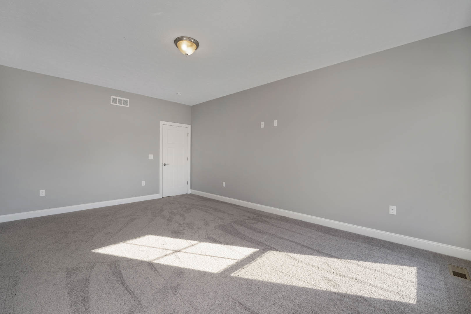 White paneled door with silver handle, beige carpeted floor, white plaster walls, ceiling light fixture, sunlight casting window shadow across floor