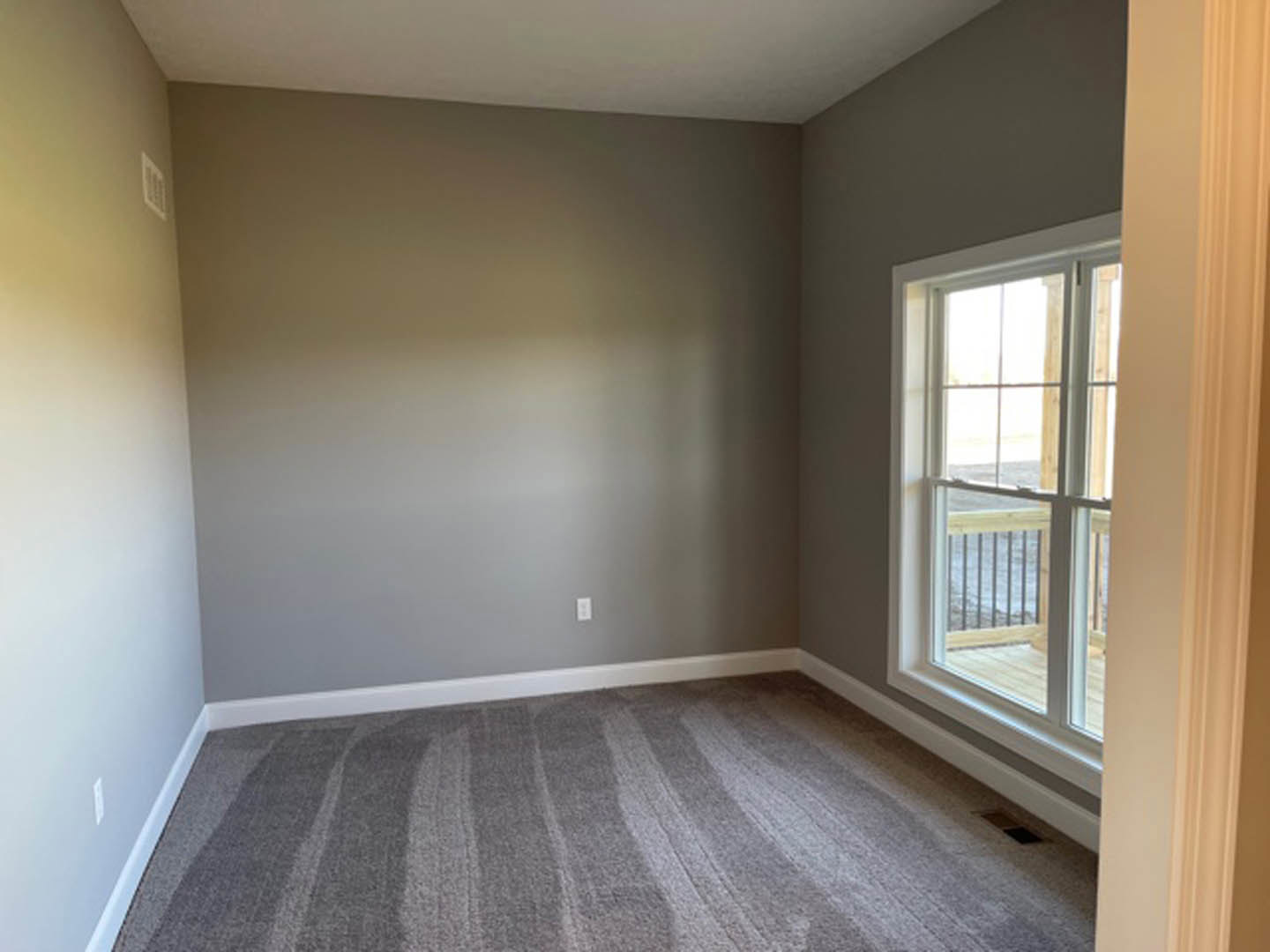 Carpeted bedroom with white plaster walls, large window featuring wood trim and metal railing