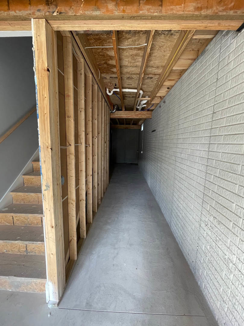 Hallway with exposed wood ceiling beams, white brick accent wall, wooden staircase, and contrasting black and white doors