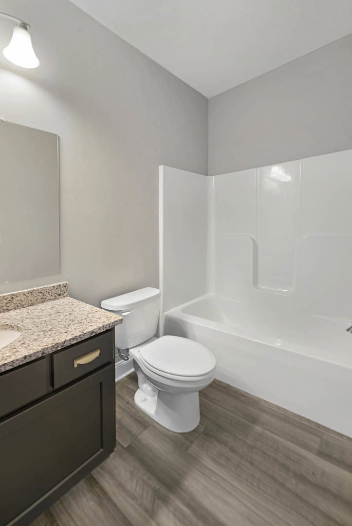Modern bathroom with white toilet, freestanding bathtub, light tile flooring, and white walls; black vanity drawer and chrome plumbing fixtures visible