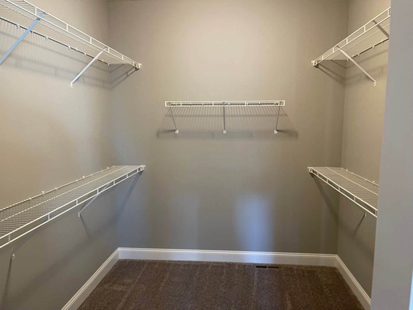 Walk-in closet with white metal shelving, hanging rods, and light-colored carpet flooring