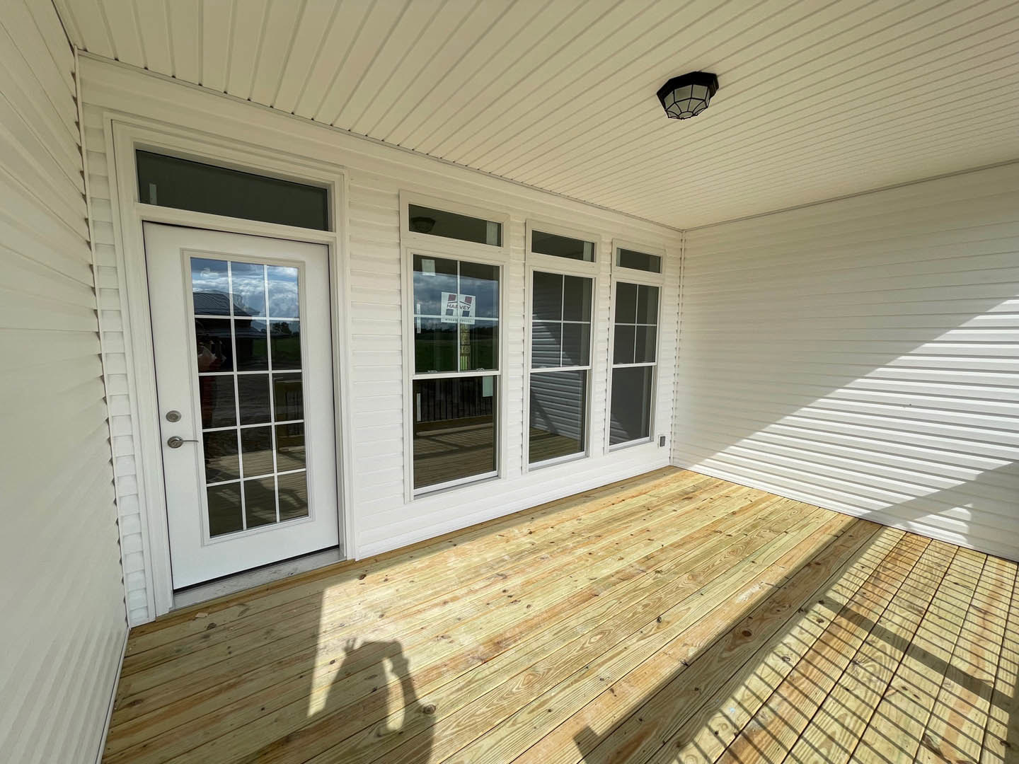 White exterior home with wood deck, glass panel door, large windows, and light fixture visible near entrance