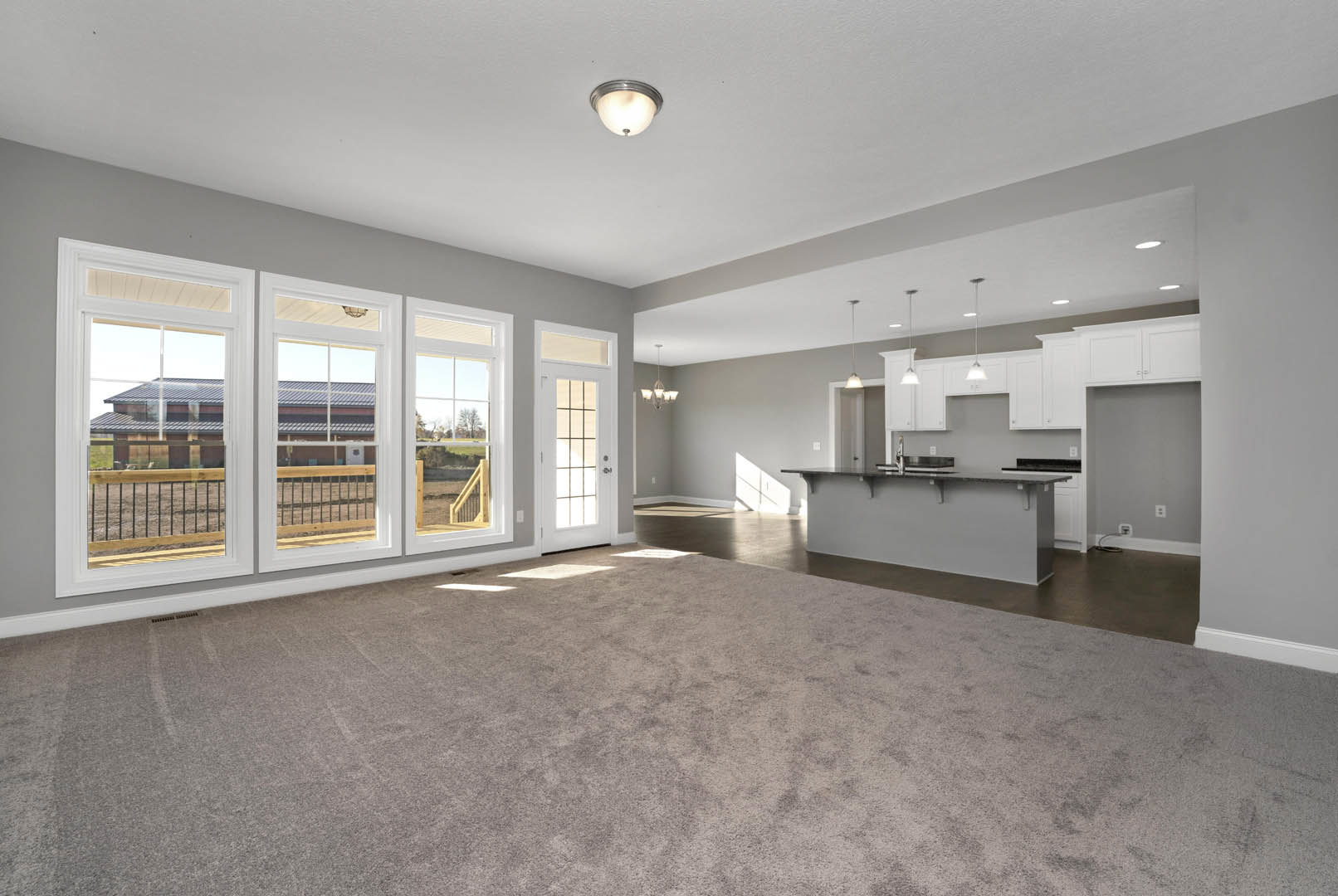 Spacious living room with carpet flooring, open kitchen featuring cabinetry and a bar, pendant light fixture on ceiling, row of large windows, countertop with sink and faucet