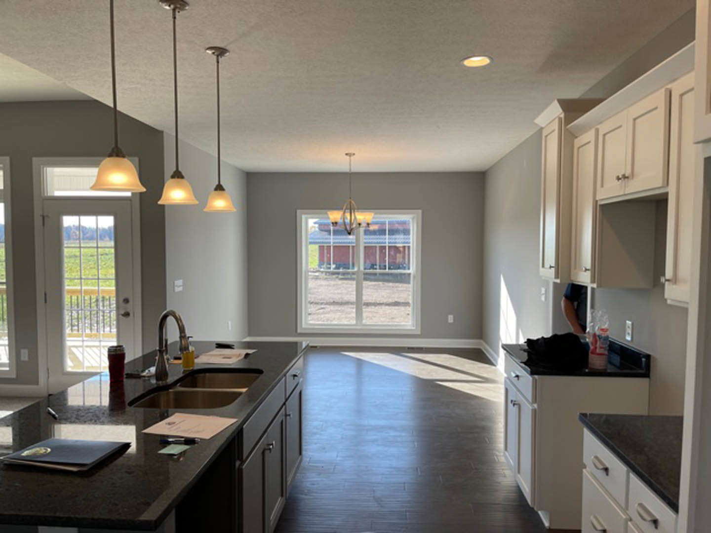 Modern kitchen featuring white cabinetry, stone countertops, stainless steel sink, large window with natural light, pendant ceiling lights, and light-colored walls