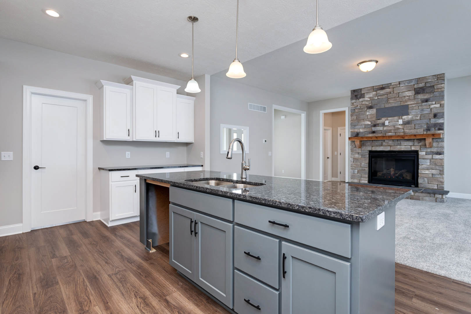 Kitchen with granite countertops, white cabinetry, stainless steel sink, stone fireplace with glass door, white door with black handle, round ceiling light fixture, hardwood