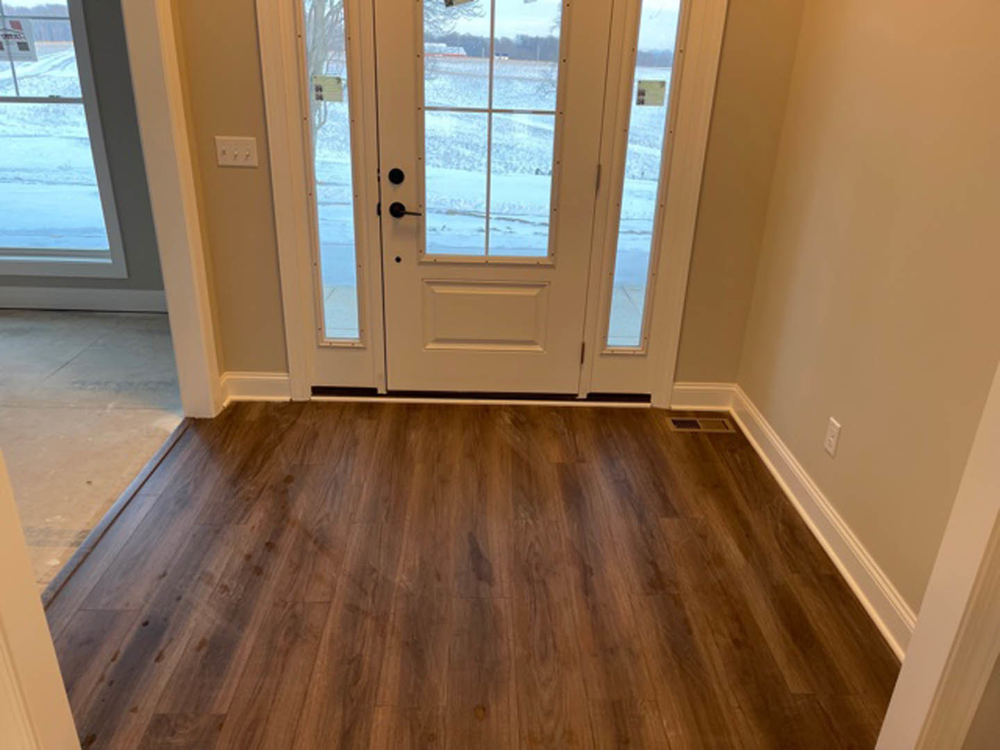 Hardwood floor in a room with white walls, a white door with glass panes, and windows overlooking a snowy landscape