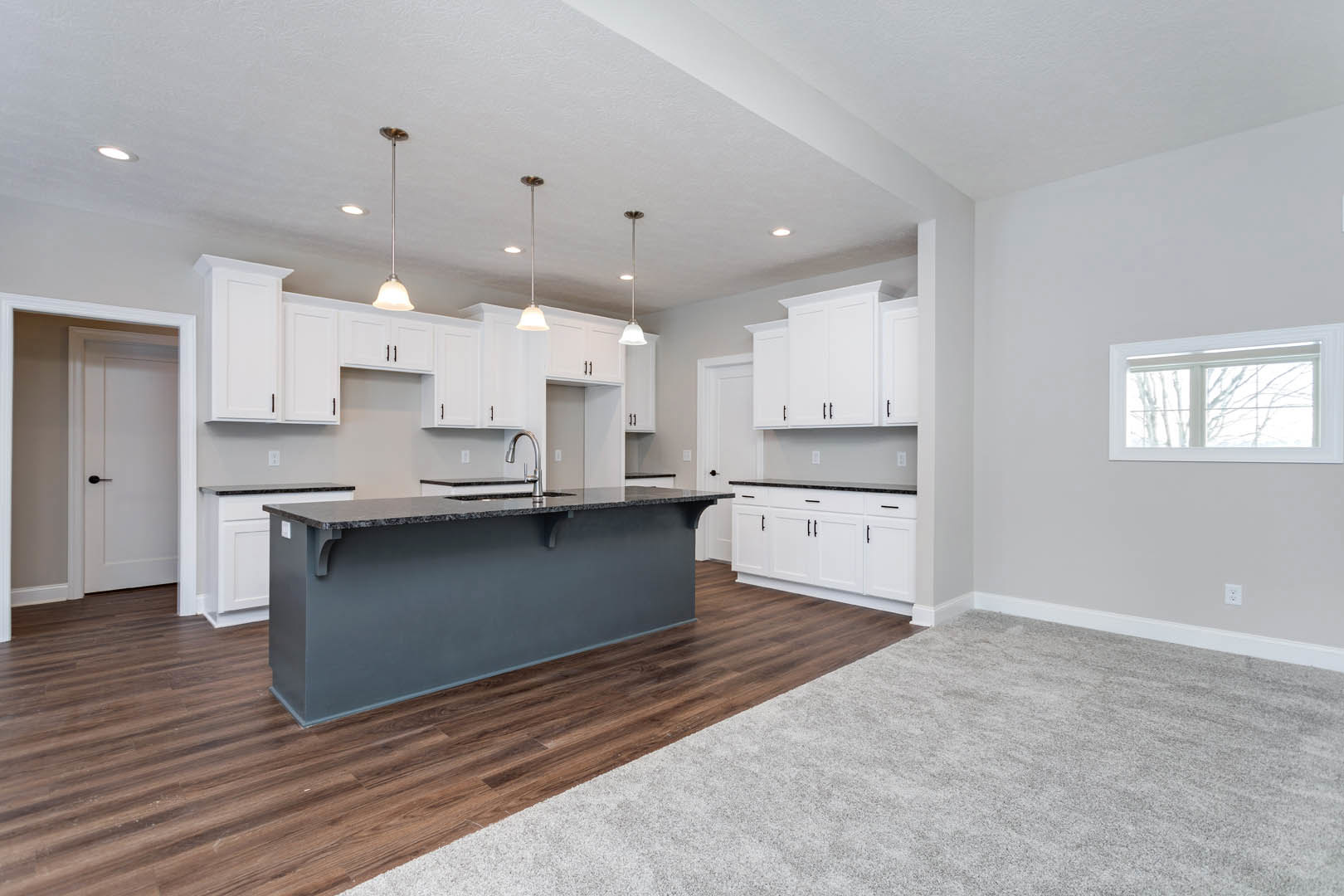 Black kitchen island with waterfall countertop, white cabinetry, wood flooring, white-framed window, and white door with black handle.