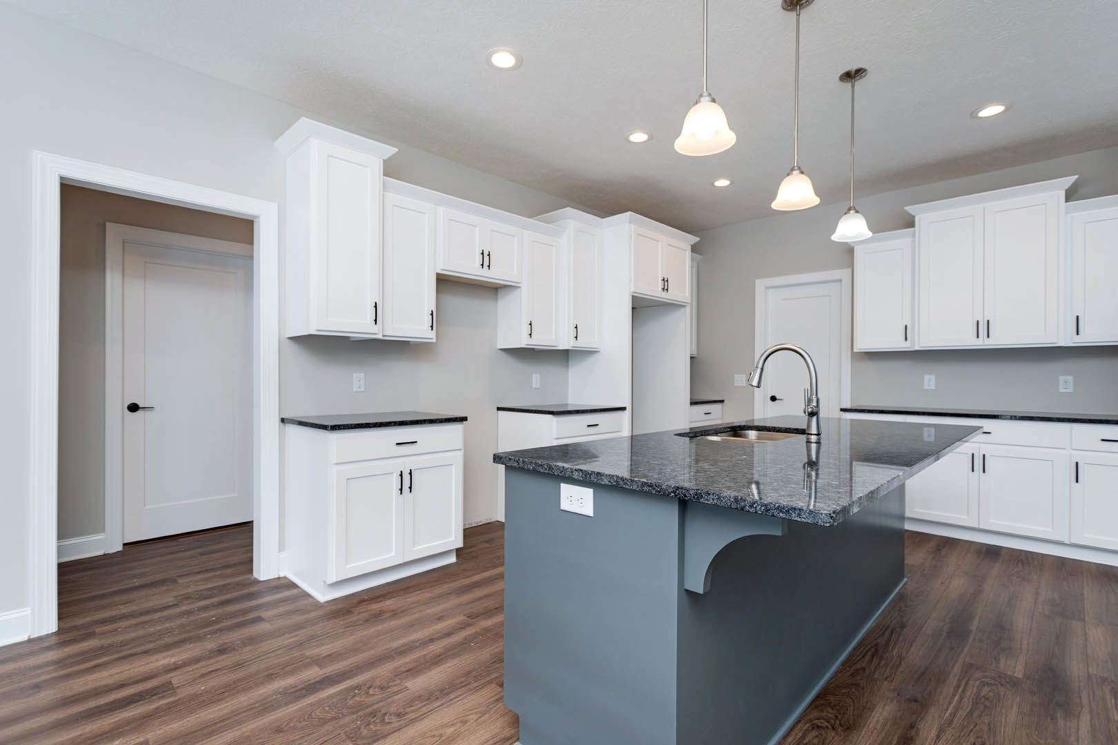 Spacious kitchen featuring a large central island with built-in sink, white cabinetry with black countertops, stainless steel appliances, and a white door with black handle.