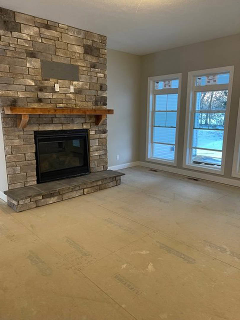 Fireplace with glass door and wood mantel, brick hearth with stone step, two windows with white trim, hardwood flooring