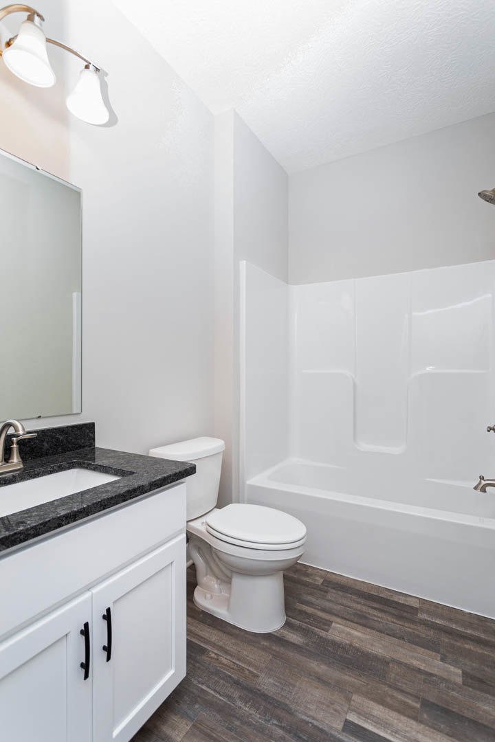 Modern bathroom with white porcelain sink and toilet, light gray tile flooring, chrome faucet, and wall-mounted light fixture above a white vanity.