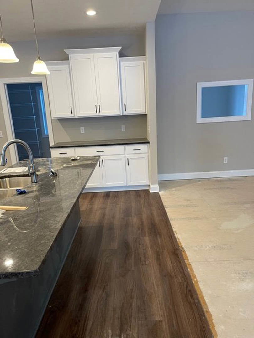 Marble countertop with undermount sink, wood flooring, white cabinetry, stainless steel faucet, and tiled backsplash in a modern kitchen