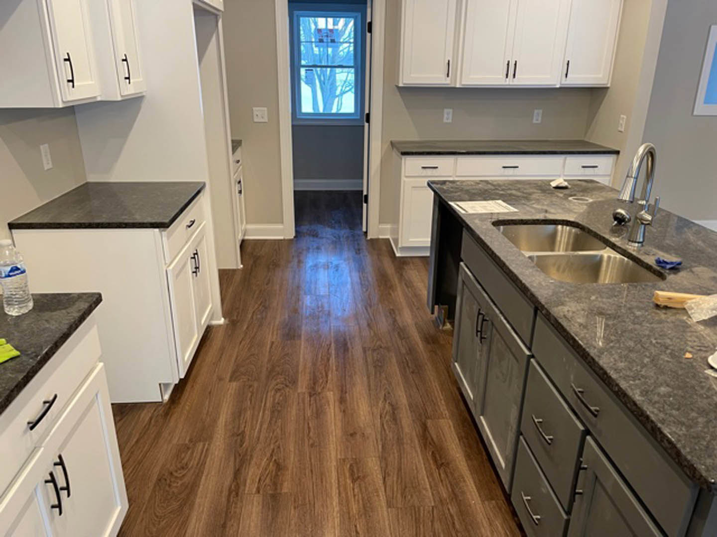 White kitchen cabinets with black countertops, stainless steel sink, wood flooring, and under-cabinet lighting.